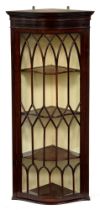 An Edwardian serpentine mahogany hanging corner cabinet, the glazed door with lancet and diamond