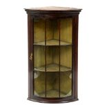 A bow fronted mahogany hanging corner cabinet, early 20th c, with dentil cornice and glazed nine