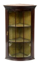 A bow fronted mahogany hanging corner cabinet, early 20th c, with dentil cornice and glazed nine