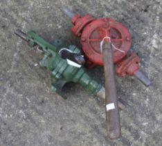 Two vintage hand water pumps. In green and red, with wooden handles.