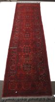 A Persian style red wool runner rug. With a black geometric border and central design.