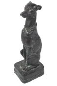 A Faux bronze and resin sculpture of a greyhound. In a seated positon, wearing a chain link collar.