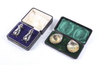 Two pairs of silver cruets in boxes including a pair of shell shaped salts on ball feet.