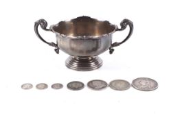 A silver small two handled trophy bowl on foot and various silver coins.