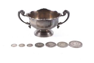 A silver small two handled trophy bowl on foot and various silver coins.