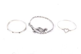 Three white metal bangles including a cross-over example in the form of a dragon.