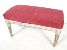 A pink upholstered footstool. With a carved wooden frame and turned tapering fluted supports.