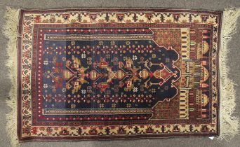 A Turkish prayer rug with various motifs below arches pointing towards the buildings of Mecca.