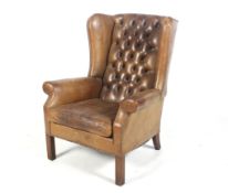 A Georgian style button back brown leather wingback armchair.