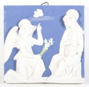 A white and blue glazed terracotta wall plaque depicting Mary visited by the angel.