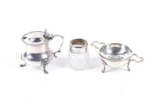 A silver mustard pot, silver rimmed dressing table jar and a silver-plated tea strainer.