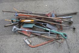 A collection of assorted garden hand tools. Including spades, hoes, forks and a bow saw.
