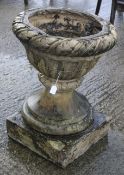 A large reconstituted stone garden urn. On a square plinth.