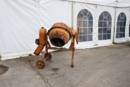 A vintage orange electric cement mixer. On a wheeled stand.