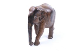 A 20th century hand carved Indian hardwood elephant figure. Striding, with trunk pendant.