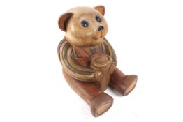 A 1970s German carved wood 'Paddington' style seated bear. Holding a pot and wearing dungarees.