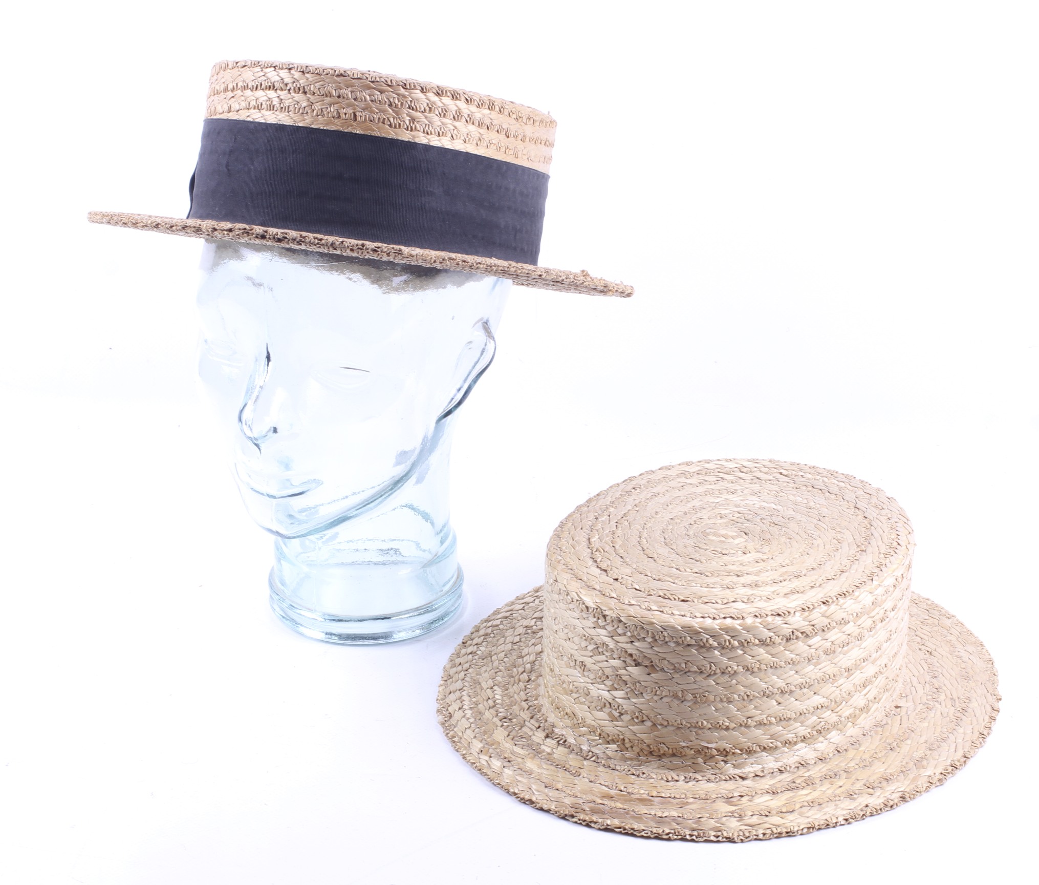 Two vintage straw boater hats and a glass headstand.