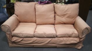 A three seater sofa with coral pink upholstery.