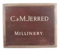 A vintage metal advertising sign for 'C. & M. Jerred Millinery'. Produced by H.B.