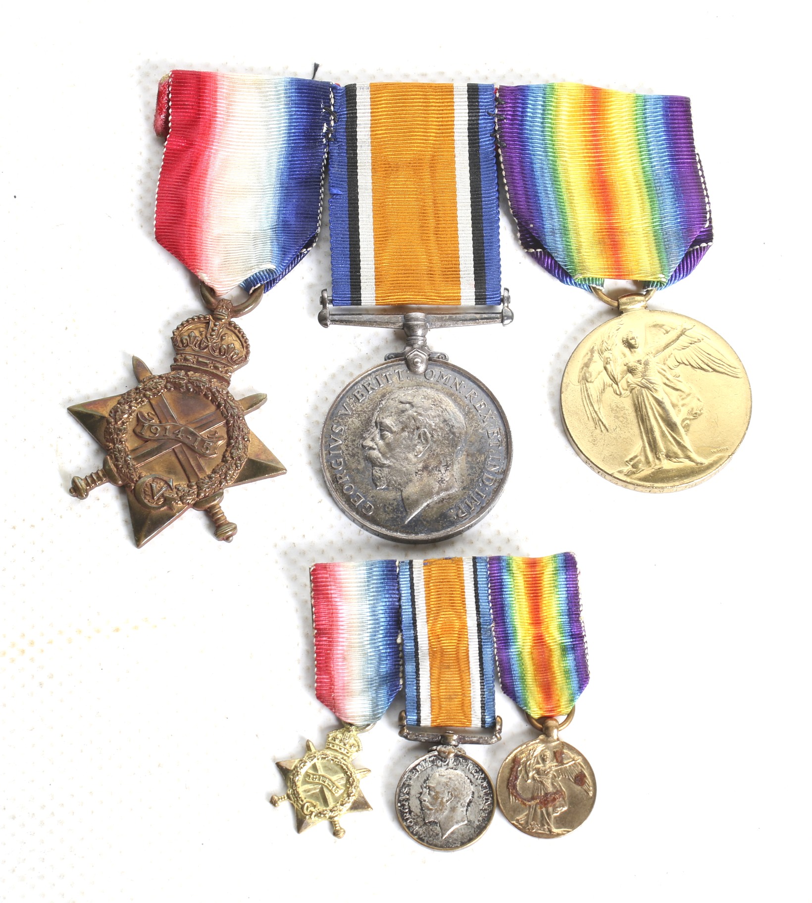 A set of three WWI medals and miniatures, a ship insignia and a cap badge.