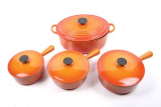 Four pieces of Le Creuset orange pans.