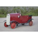 A circa 1930s tin plate pedal car. Red body with black trim and red wheels, H49cm x L77cm.