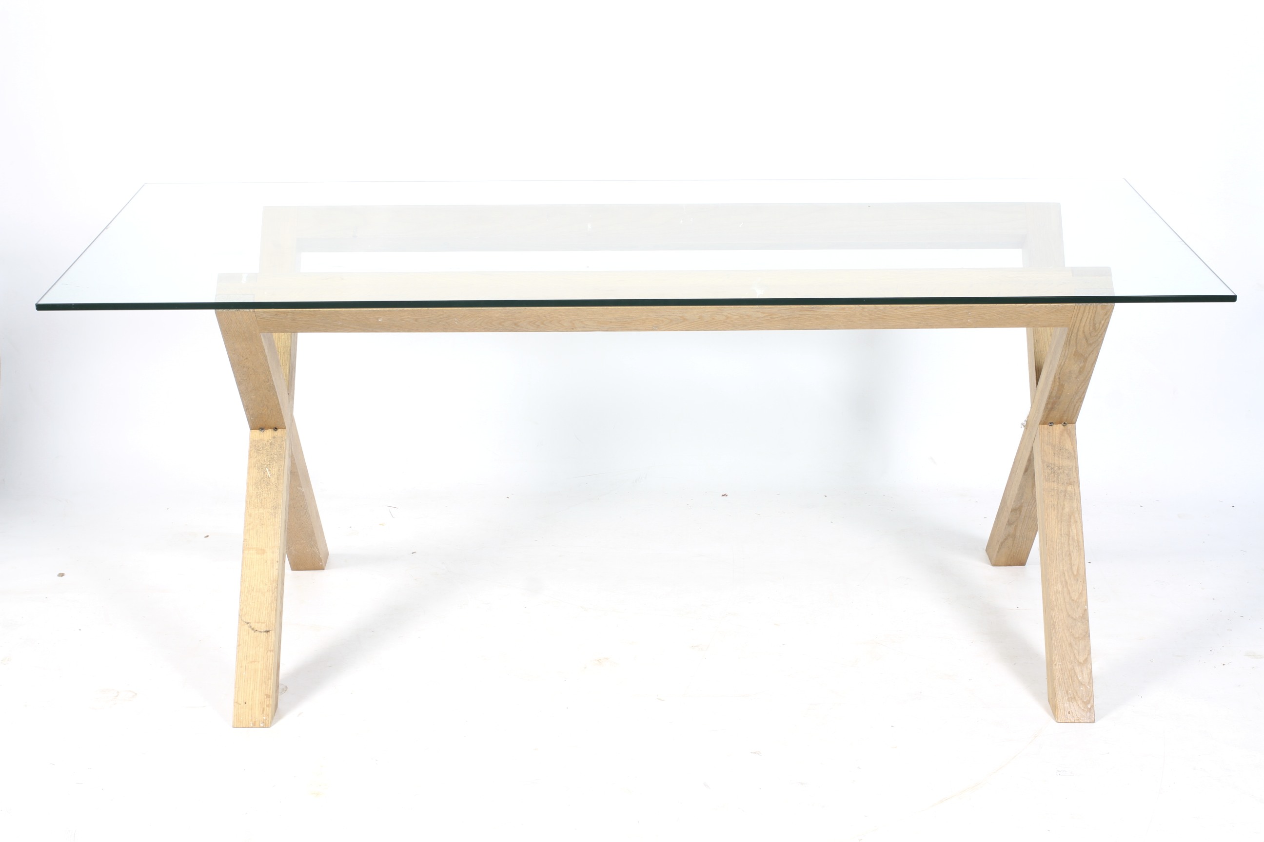 A contemporary glass top dining table. With a wooden X-frame support.