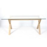 A contemporary glass top dining table. With a wooden X-frame support.