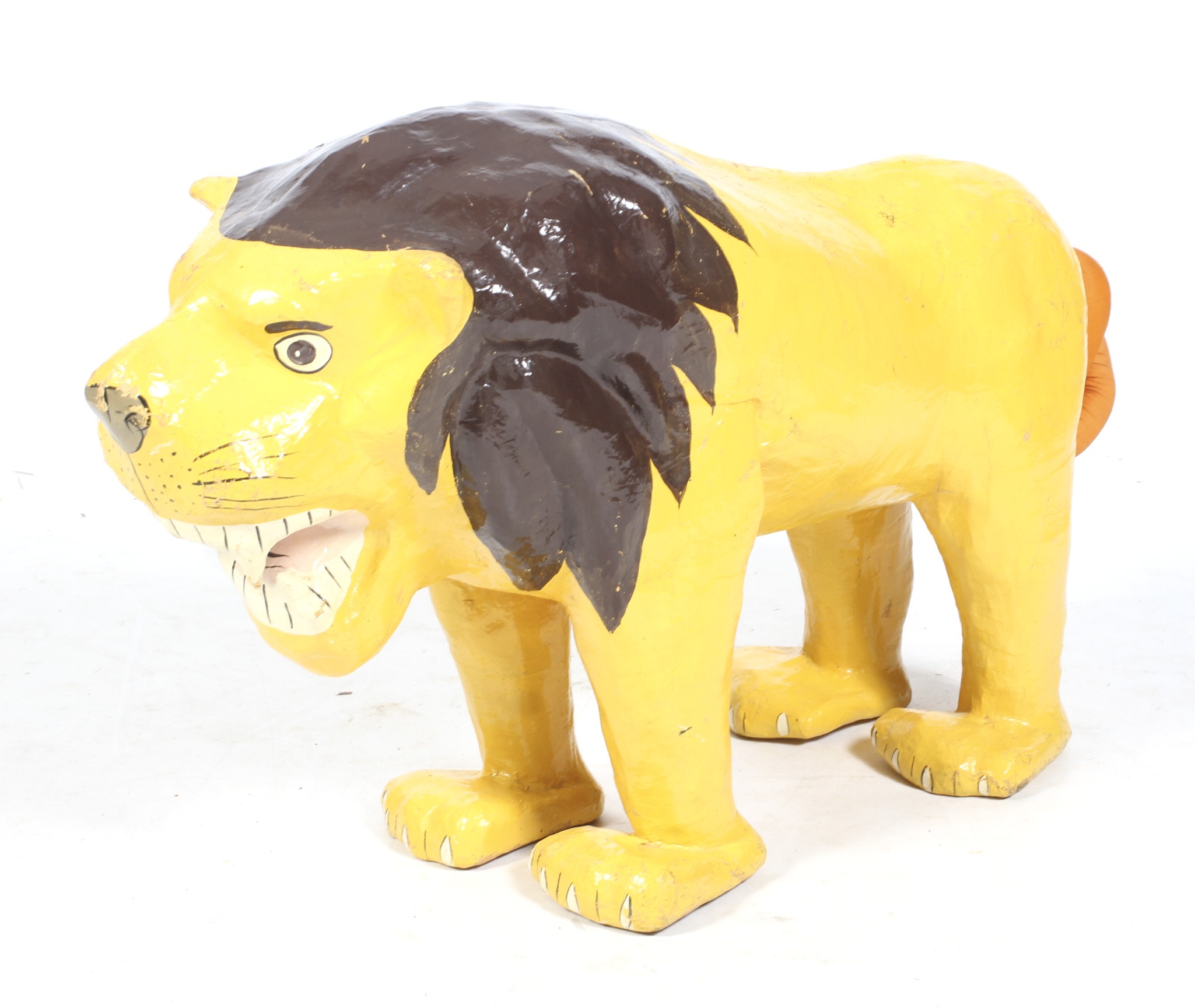 A large painted papier mache lion. WIth open jaws, standing square, with a stuffed fabric tail.