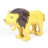 A large painted papier mache lion. WIth open jaws, standing square, with a stuffed fabric tail.