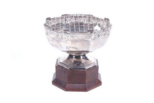 A silver octagonal rose bowl with a wire-work mesh and on an oak stand.