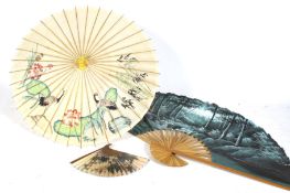 A large Asian painted fan, a parasol, and a small Chinese fan.