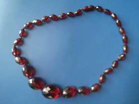 A red amber coloured necklace comprising graduated faceted oval beads, 19".