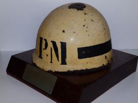 A holed Argentinian Falklands War presentation Military Police helmet, fixed to a wooden base with