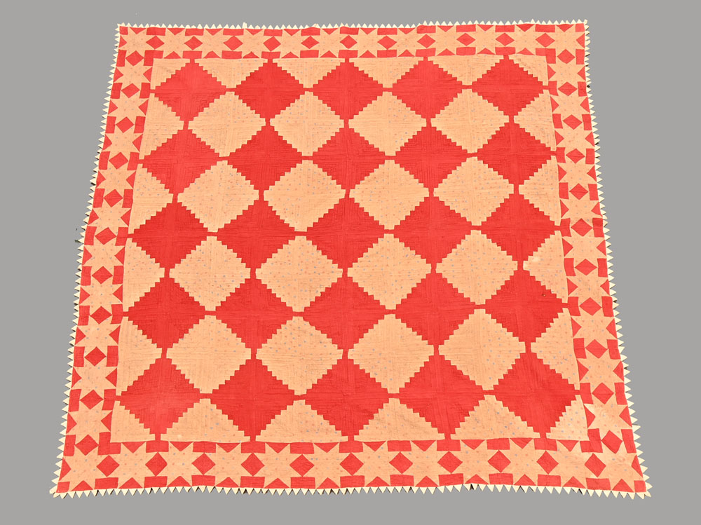 A patchwork quilt in red and beige, lined to back and edged with dogtooth points. 240 cm square.