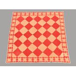 A patchwork quilt in red and beige, lined to back and edged with dogtooth points. 240 cm square.