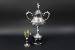 Two hound trailing trophies, the first with classical finial and with twin handles,