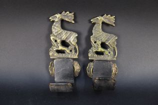 A pair of brass and leather gun wall hanging mounts, decorated with stag and hounds,