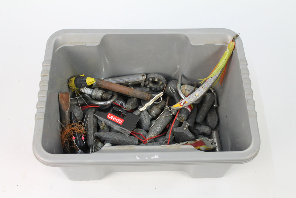 A plastic tub containing a large quantity of sea fishing weights, pirks etc.