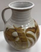 An Alan Caiger-Smith Aldermaston Pottery jug with ochre glaze and scrolling design on a white