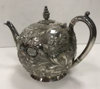 A Victorian silver bullet-shaped tea pot with all over floral and foliate embossed decoration (by