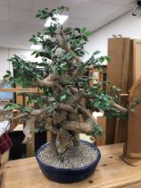 A faux Bonsai tree of large proportions on a gravel topped blue pottery bowl base,