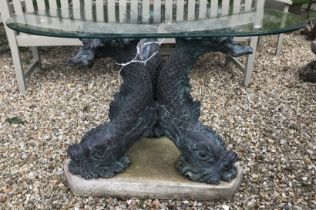 A glass top garden table on 3 stylised dolphin supports to a fibreglass base 120 x 80 x 69 cm high