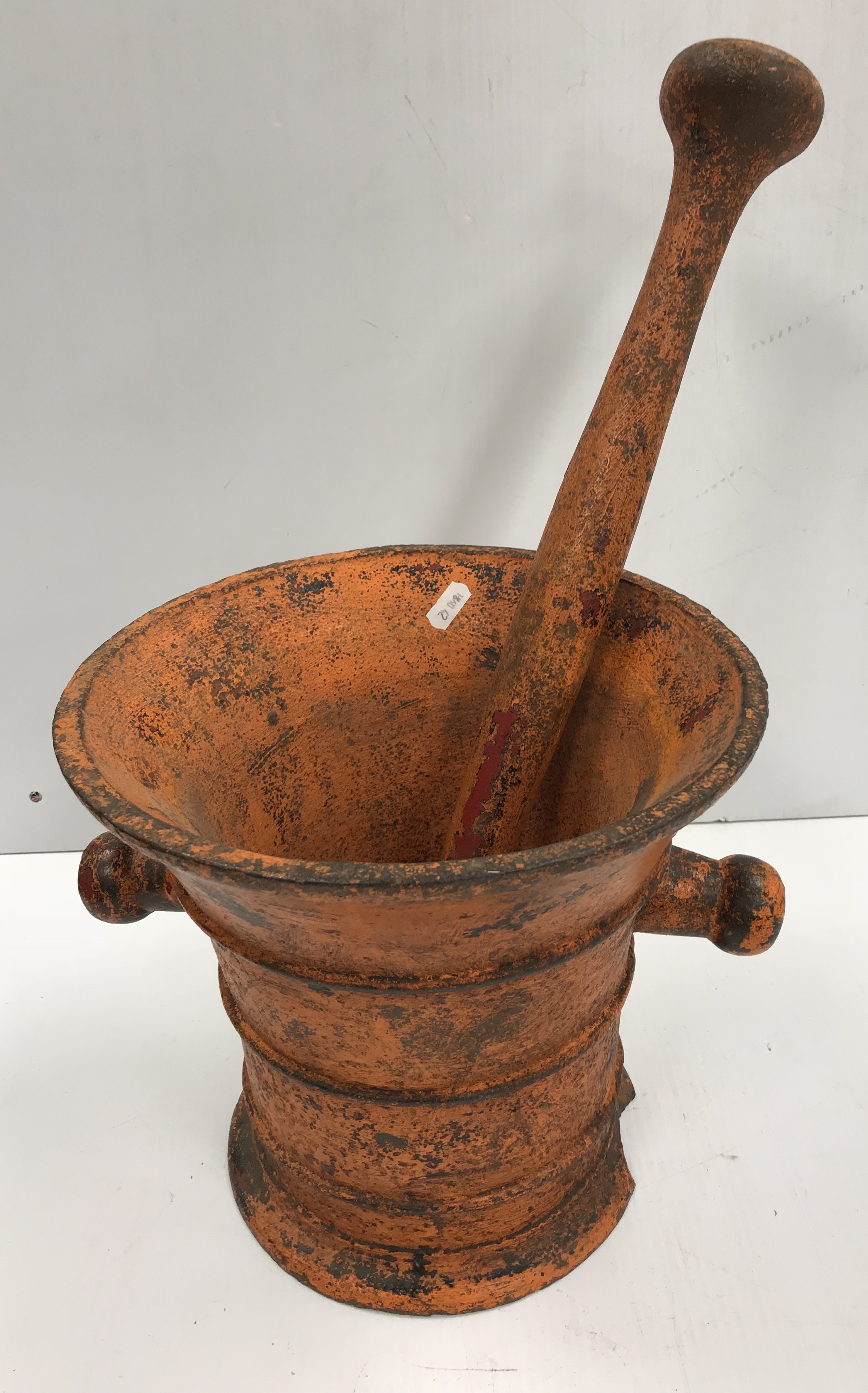 An orange painted cast iron pestle and mortar of large proportions, the mortar 27.