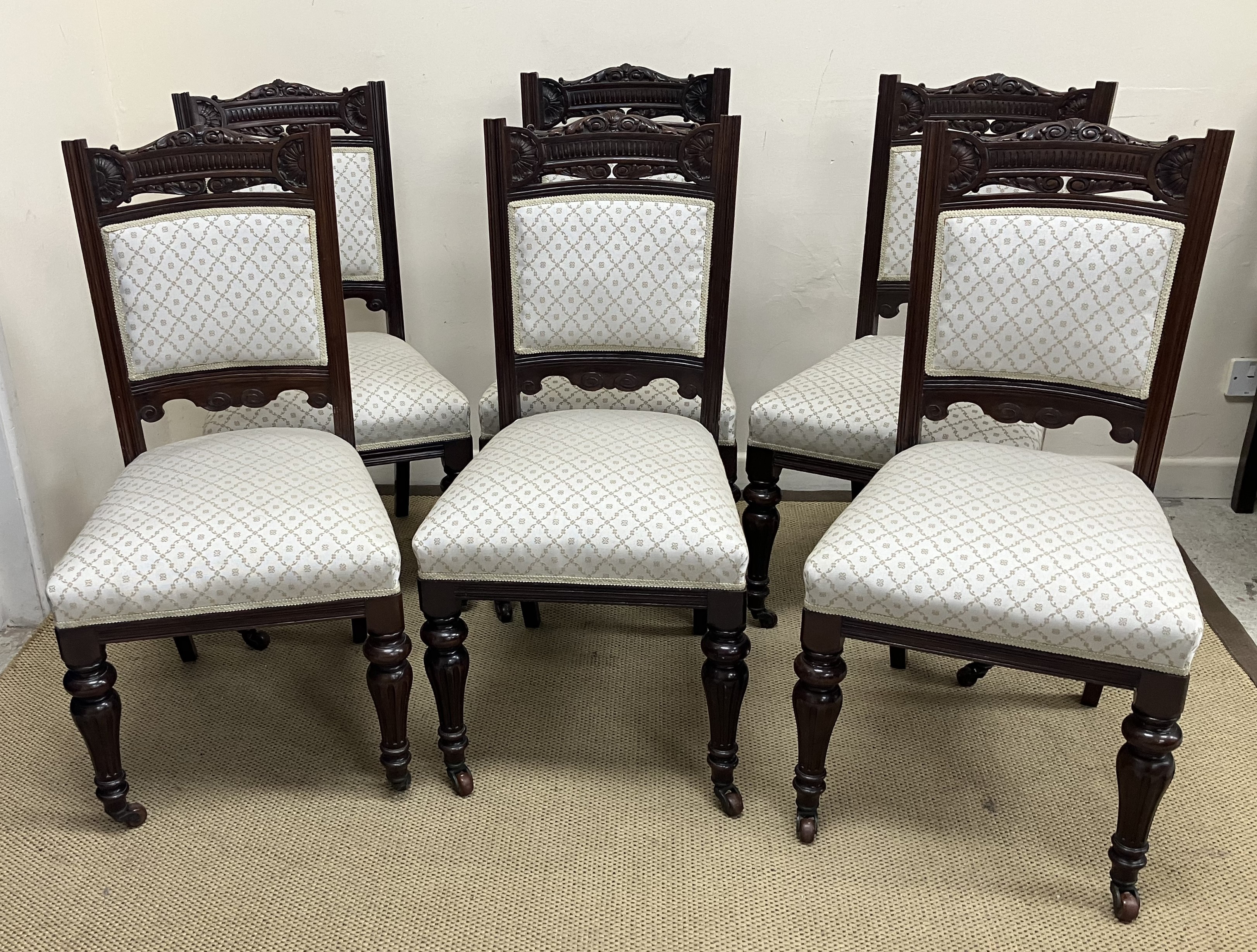 A set of six late Victorian carved mahogany framed dining chairs with upholstered back panels and