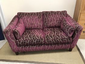 A modern two seat sofa with purple and mushroom foliate decorated upholstery raised on square