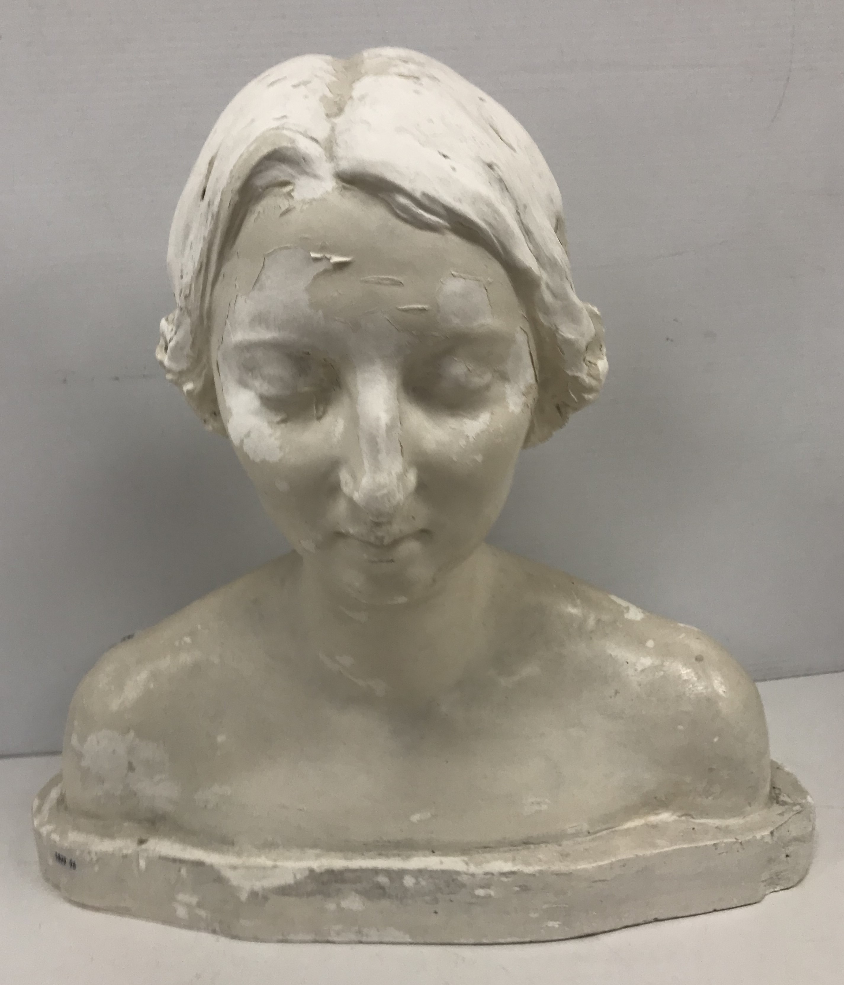 A white painted plaster bust portrait sculpture of a young woman, eyes closed,