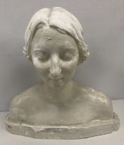 A white painted plaster bust portrait sculpture of a young woman, eyes closed,