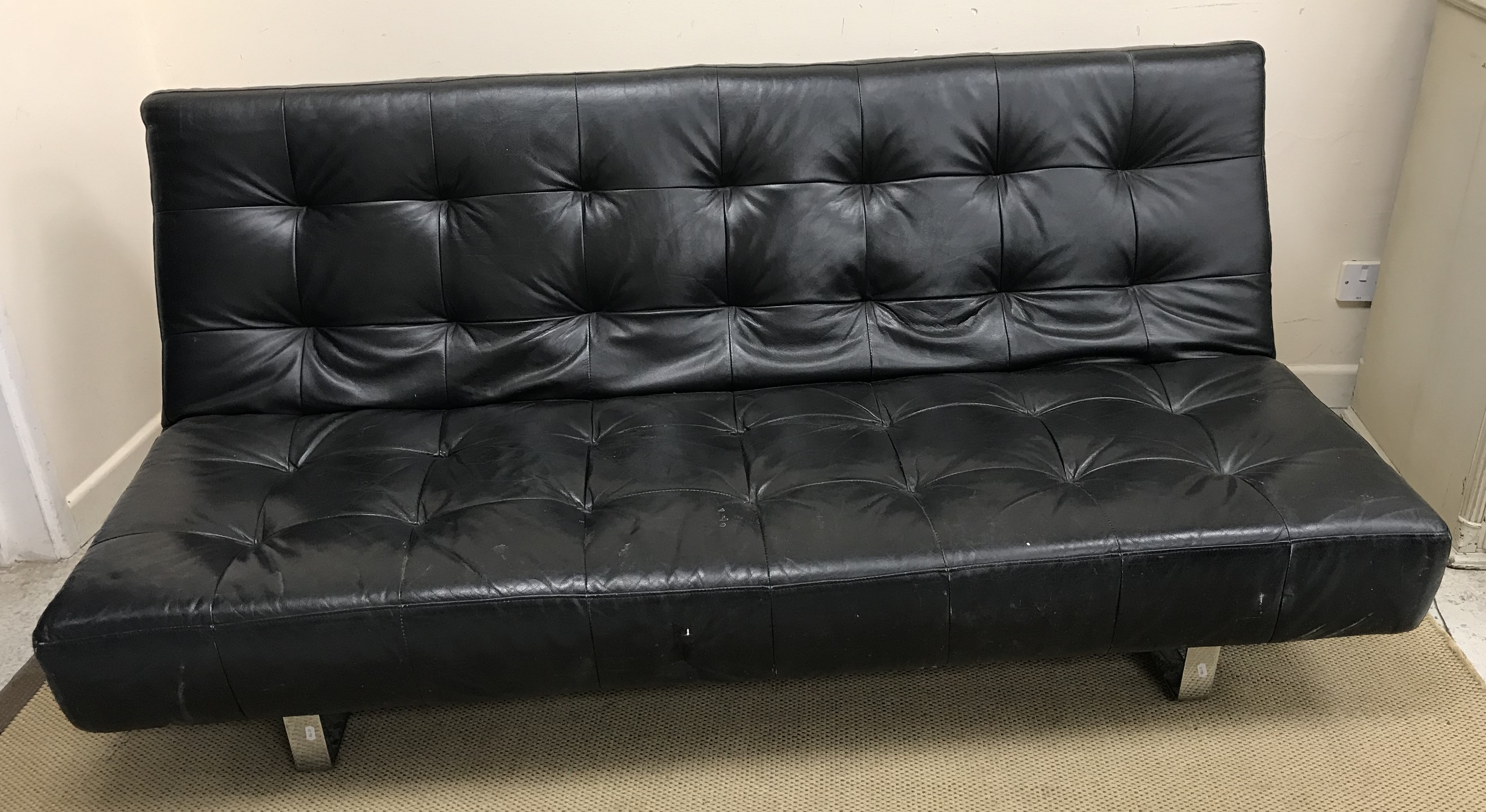 A modern black leather sofa on chromed legs, the back folding down to convert to a bed,