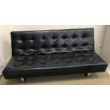 A modern black leather sofa on chromed legs, the back folding down to convert to a bed,